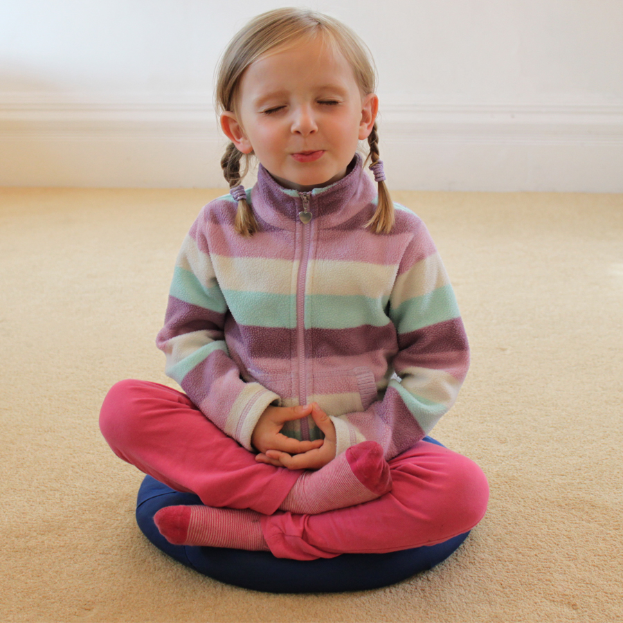 A cute little girl in a stripy top and pink pants meditating