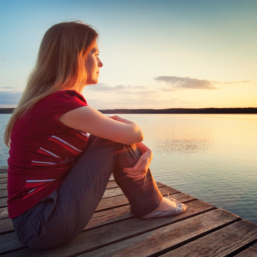 Young woman on pier at sunset, looking happy, looking across water