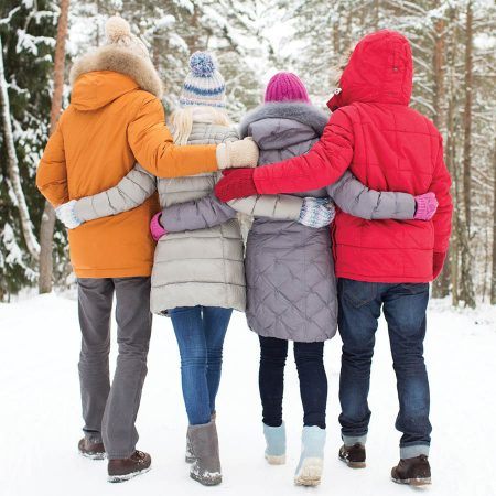Four friends walking arm-in-arm on snowy road in countryside