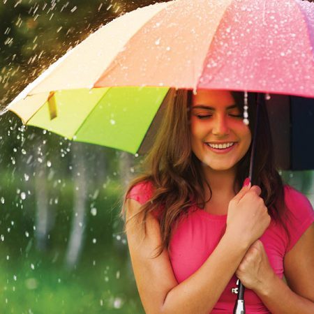 Young woman smiling in the rain, under a colourful umbrella