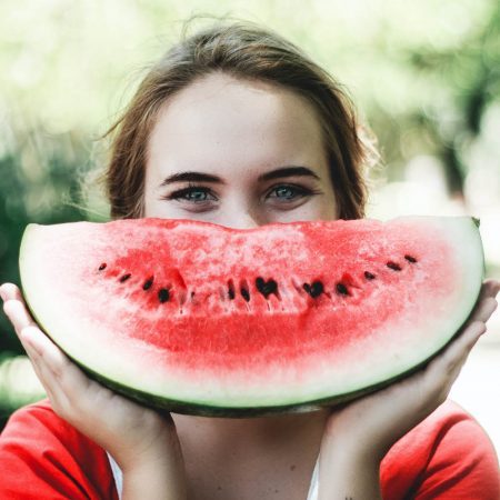 Young woman smiling, holding up slice of watermelon